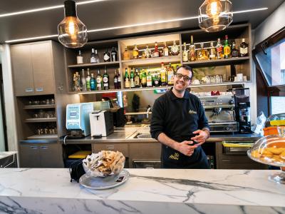 Luca, con il suo sorriso contagioso, è dietro al bancone di Attimi Bar. Qui ha l’occasione di mettersi in gioco in un ambiente accogliente, dove ogni gesto porta verso l’autonomia e racconta il valore dell’inclusione. Il bar è della Cooperativa iSemprevivi, che si occupa di inserimento lavorativo: dal 2021 sono stati assunti 12 ragazzi con fragilità psichiatrica.
